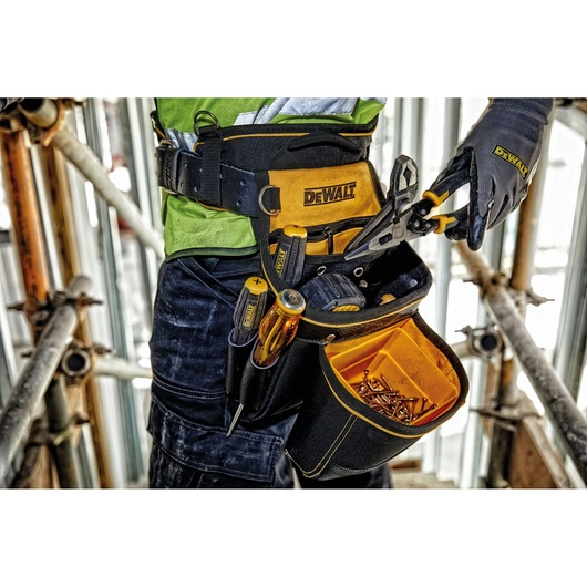DEWALT tool belt with pouch, tools, and screws. Person wears gloves, ready for work at a construction site.
