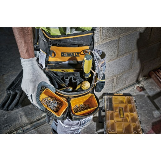 DEWALT tool belt with compartments holding screws and tools, worn by a worker with gloves near a DEWALT case.