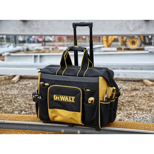 DEWALT rolling tool bag with yellow and black design, filled with tools, shown at a construction site.