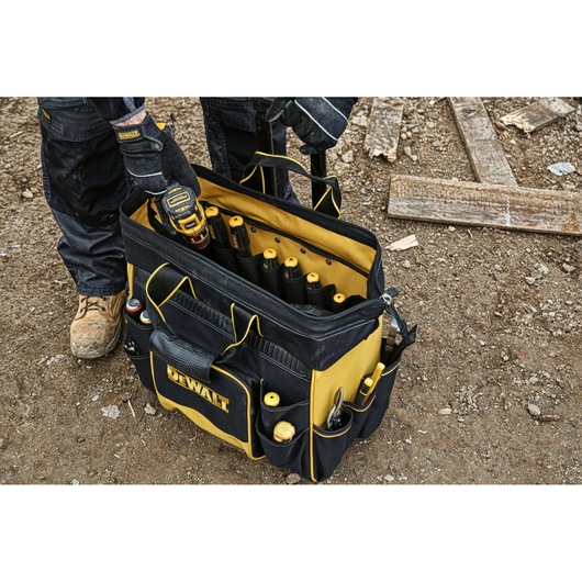DEWALT toolbag filled with tools on a construction site, with a worker wearing gloves using the bag.