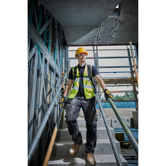 Worker in safety gear on stairs at construction site with DEWALT vest and helmet.